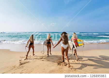Four women holding surfboards run on tropical beach towards ocean waves. Bikini sport lovers enjoy surfing adventure, explore seaside holiday spot. Friends bond in surf trip, summer travel fun. Four women holding surfboards run on tropical beach towards ocean waves. Bikini sport lovers enjoy surfing adventure, explore seaside holiday spot. Friends bond in surf trip, summer travel fun. 126895861