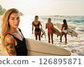 Blonde girl with surfboard on sunny beach. Women in swimsuits with surfboards by ocean. Golden sand, sunset waves. Surf lifestyle, summer vibes, water sports, active vacation, outdoor adventure. 126895871