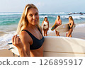 Group of women on sandy beach learn surfing. Female group holds surfboards by ocean. Surf school for beginners on sunny coastline. Summer day at seaside sports lessons. 126895917