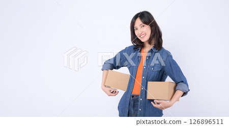 Southeast asian woman in denim shirt smiling and holding two cardboard boxes against white background, showing cheerful and confident expression suitable for delivery or moving concept Southeast asian woman in denim shirt smiling and holding two cardboard boxes against white background, showing cheerful and confident expression suitable for delivery or moving concept 126896511
