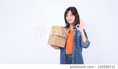Southeast asian woman holding cardboard boxes shows ok gesture while enjoying internet online shopping experience with cheerful smile on white background Southeast asian woman holding cardboard boxes shows ok gesture while enjoying internet online shopping experience with cheerful smile on white background 126896512