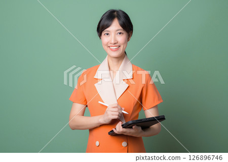 Southeast asian woman in orange dress holding digital tablet and stylus smiling confidently against green background 126896746