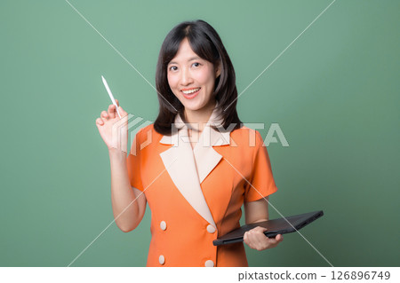 Southeast asian woman smiling confidently while using internet technology holding digital tablet and stylus pen against green background 126896749