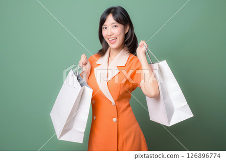 Southeast asian woman smiling while holding shopping bags showing excitement for internet online shopping against green background 126896774