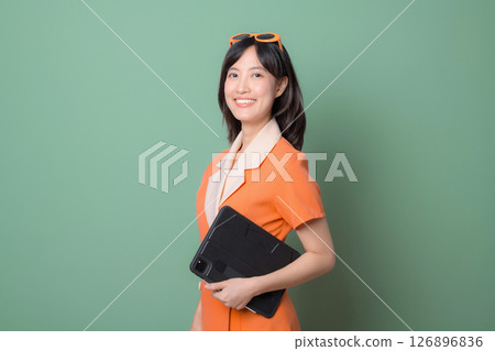 Southeast asian woman in orange dress holding tablet smiling confidently against green background modern style 126896836