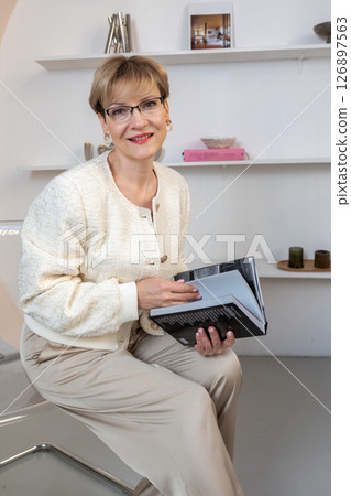 Portrait of smiling woman with glasses and book in her hands in bright room. Vertical photo. High quality photo 126897563