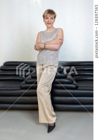 Smiling woman in festive clothes standing near black sofa in bright room. Vertical photo. High quality photo Smiling woman in festive clothes standing near black sofa in bright room. Vertical photo. High quality photo 126897565