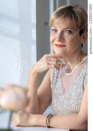 Portrait of smiling woman in festive clothes against a gray wall in a bright sunny room. Vertical photo. High quality photo Portrait of smiling woman in festive clothes against a gray wall in a bright sunny room. Vertical photo. High quality photo 126897569