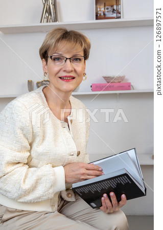 Portrait of smiling woman with glasses and book in her hands in bright room. Vertical photo. High quality photo 126897571