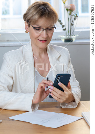 Portrait of business woman. Confident mature woman using mobile phone and typing. Vertical photo. High quality photo 126897622