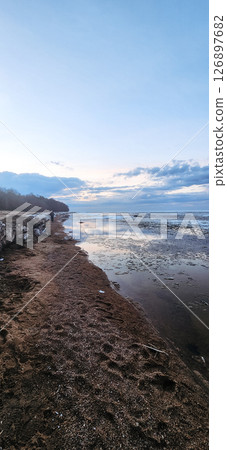 Spring landscape. Panoramic view of beautiful dawn on bay. Cumulus clouds over water in bright light. Ice, snow and rocks on coastline. Rising rays of sun are reflected in sea. Vertical photo. Spring landscape. Panoramic view of beautiful dawn on bay. Cumulus clouds over water in bright light. Ice, snow and rocks on coastline. Rising rays of sun are reflected in sea. Vertical photo. 126897682