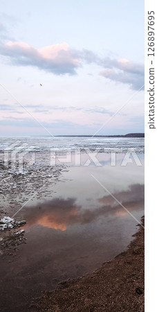 Spring landscape. Panoramic view of beautiful dawn on bay. Cumulus clouds over water in bright light. Ice, snow and rocks on coastline. Rising rays of sun are reflected in sea. Vertical photo. Spring landscape. Panoramic view of beautiful dawn on bay. Cumulus clouds over water in bright light. Ice, snow and rocks on coastline. Rising rays of sun are reflected in sea. Vertical photo. 126897695