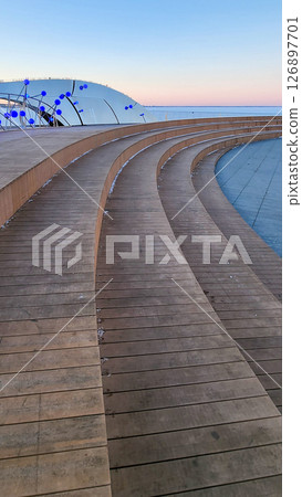 stylish boardwalk featuring a contemporary architectural design with striking blue light spheres. Reflective surfaces enhance the structure against a clear sky backdrop 126897701