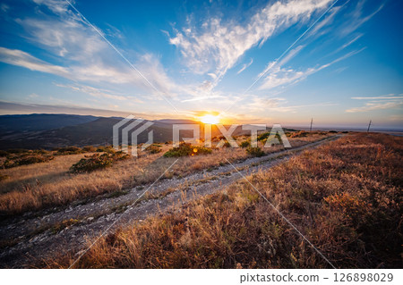 Sunset illuminating Crimean mountains and steppe landscape with a gravel road 126898029