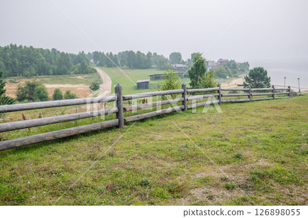 Scenic view of russian countryside with wooden fence, dirt road, forest, village and river in foggy morning 126898055