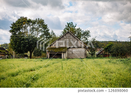 Old abandoned wooden barn standing in green field under cloudy sky Old abandoned wooden barn standing in green field under cloudy sky 126898060