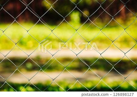 Metal mesh fence separating green grass from the rest of the world 126898127