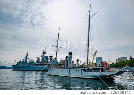 Russian warships, including a vintage ship and a modern one, are docked in a harbor on a cloudy day 126898142