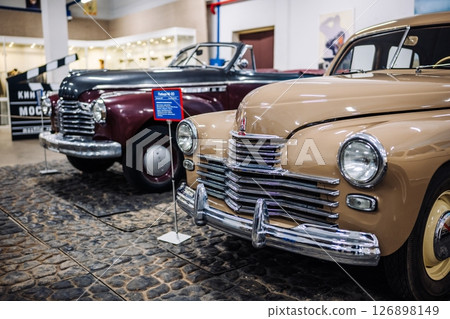 Beige Pobeda car showing in front of a vintage maroon car in a museum Beige Pobeda car showing in front of a vintage maroon car in a museum 126898149
