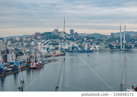 Cranes, cargo ships, and russian navy warships fill the foreground of golden horn bay, with vladivostok's skyline rising behind Cranes, cargo ships, and russian navy warships fill the foreground of golden horn bay, with vladivostok's skyline rising behind 126898171