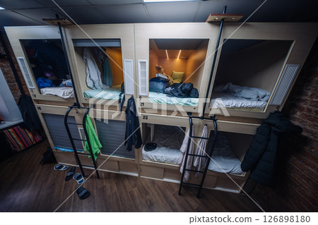 Capsule hotel beds showing clothes and bags hanging, offering affordable accommodation Capsule hotel beds showing clothes and bags hanging, offering affordable accommodation 126898180
