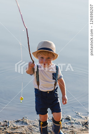 A small toddler boy standing by a lake at sunset. Copy space. 126898207