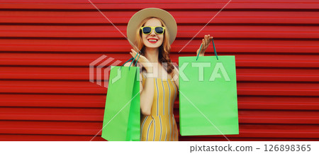 Stylish beautiful happy woman standing with colorful shopping bags posing on vivid red wall Stylish beautiful happy woman standing with colorful shopping bags posing on vivid red wall 126898365
