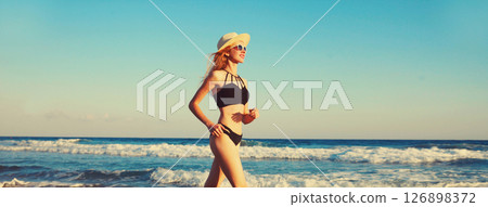Summer vacation, happy slim woman walking running in bikini, tourist hat on the beach on sea coast Summer vacation, happy slim woman walking running in bikini, tourist hat on the beach on sea coast 126898372