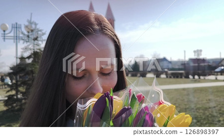 Young woman in a park smelling a bouquet of yellow and purple tulips. young woman with tulips in the park Young woman in a park smelling a bouquet of yellow and purple tulips. young woman with tulips in the park 126898397