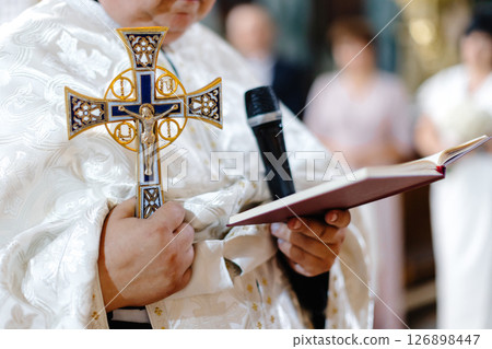 Priest Holding Cross and Reading from Holy Book during Ceremony Priest Holding Cross and Reading from Holy Book during Ceremony 126898447