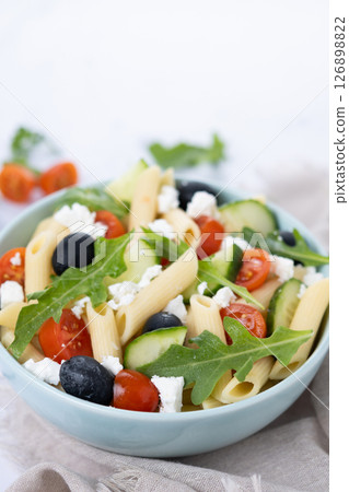 Mediterranean Pasta Salad in bowl with Fresh Vegetables and Herbs on green background 126898822