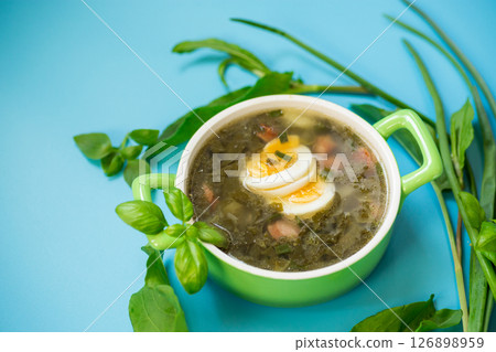 Homemade green borscht with boiled egg and fresh sorrel on top on a blue background 126898959
