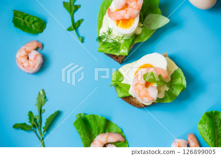Appetizing breakfast with shrimp, egg and greens on top on blue background 126899005