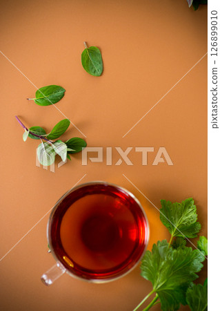 Green tea with currant leaves and mint in glass teapot and cup on brown background. Top view 126899010