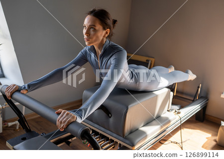 Woman doing Swan exercise on Pilates Reformer for the chest and back muscles, focusing on flexibility, strength, and control with determination 126899114