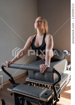 Woman training pilates on the reformer bed. Reformer pilates studio machine for fitness workouts in gym. Fit, healthy and strong authentical body. Fitness concept Woman training pilates on the reformer bed. Reformer pilates studio machine for fitness workouts in gym. Fit, healthy and strong authentical body. Fitness concept 126899123