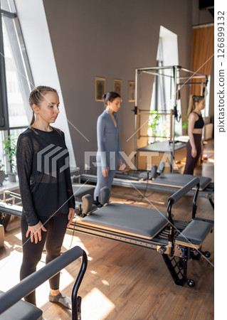 Young caucasian woman doing roll down exercise in a pilates bright studio. Their workout focuses on core strength and flexibility in a modern fitness environment. Young caucasian woman doing roll down exercise in a pilates bright studio. Their workout focuses on core strength and flexibility in a modern fitness environment. 126899132