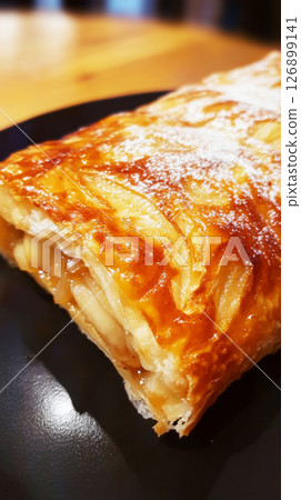 Delicious apfelstrudel served on a black plate in a cozy cafe during a sunny afternoon Delicious apfelstrudel served on a black plate in a cozy cafe during a sunny afternoon 126899141