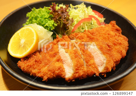 A delicious plate of crispy wiener schnitzel served with fresh lemon slices, garnished with greens, in a welcoming atmosphere of a traditional German restaurant 126899147