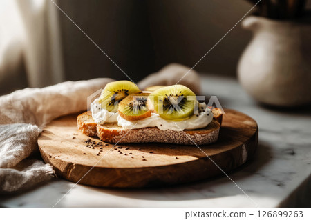 Breakfast is served with delightful toasts topped with creamy yogurt, fresh kiwi, and chia seeds on a rustic wooden plate in a warm kitchen atmosphere Breakfast is served with delightful toasts topped with creamy yogurt, fresh kiwi, and chia seeds on a rustic wooden plate in a warm kitchen atmosphere 126899263