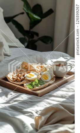 Savory pita with chicken, boiled egg, and yogurt dressing, along with a cup of hot tea, set on a white linen bed, creating a warm, cozy atmosphere with soft morning light 126899267