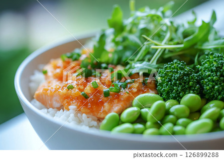 Enjoy a nutritious breakfast featuring salmon, vibrant greens, and edamame in a cozy kitchen. The bowl is garnished with sesame seeds and a slice of lemon 126899288