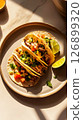 Tacos filled with shredded meat, diced tomatoes, and fresh cilantro rest on a plate beside a lime wedge in a warm, inviting ambiance, perfect for a casual meal 126899320