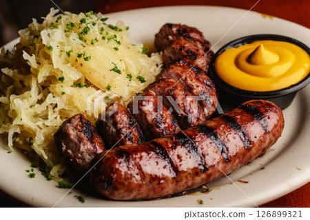 Savory bratwurst grilled to perfection alongside fresh sauerkraut and a side of mustard, served in a warm and inviting atmosphere ideal for a hearty meal 126899321