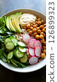 A vibrant breakfast bowl features chickpeas, sliced avocado, fresh cucumber, and radishes over grains, garnished with a dollop of sauce, perfect for a healthy start 126899323