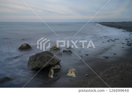 Gentle waves lap against rocky shoreline at dusk, creating a serene coastal atmosphere filled with tranquility and nature's beauty Gentle waves lap against rocky shoreline at dusk, creating a serene coastal atmosphere filled with tranquility and nature's beauty 126899648