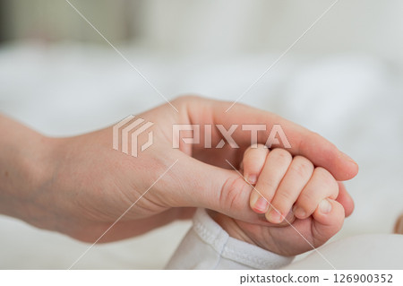 Happy family. Tiny newborn infant baby little hand on mother hand palm. Newborn baby holding parent finger after birth. Mom baby at home. Support protection of new life. Handle with care Happy family. Tiny newborn infant baby little hand on mother hand palm. Newborn baby holding parent finger after birth. Mom baby at home. Support protection of new life. Handle with care 126900352