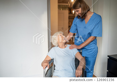 Young female nurse carrying a wheelchair with an elderly woman 126901156