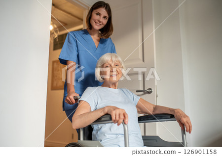 Young female nurse carrying a wheelchair with an elderly woman 126901158