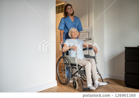 Young female nurse carrying a wheelchair with an elderly woman 126901160